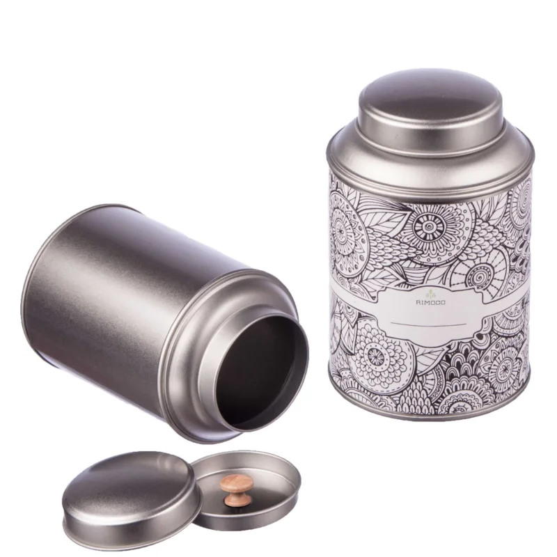 Zwei offene silberne Teedosen, eine mit Blumenmuster. Beide haben Aromadeckel und Etiketten.