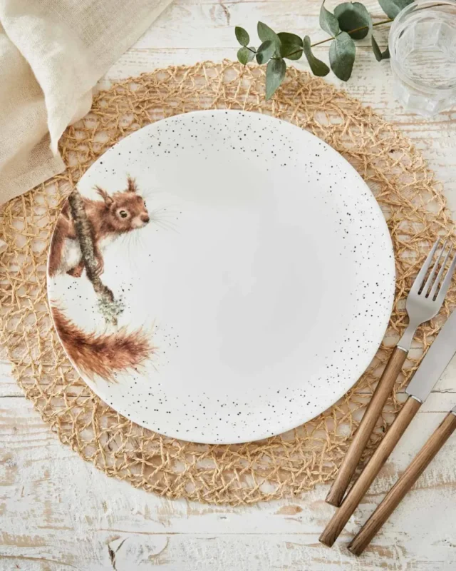 Weißer Eichhörnchen Essteller "Royal Worchester" von Wrendale Designs auf gedecktem Tisch. Auf der linken Seite des Tellers ist ein braunes Eichhörnchen zu sehen welches interessiert zum Tellerrand schaut. Der Rand des Tellers ist schwarz gepunktet. Der Teller liegt auf einem Untersetzer, neben dem Teller liegt Besteck.