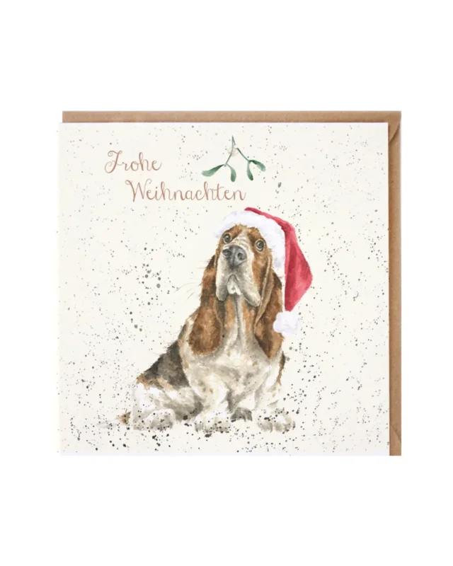 Die Doppelkarte Mistletoe von Wrendale Designs zeigt einen liebevoll illustrierten Hund mit roter Zipfelmütze unter der die langen Schlappohren des faltigen Hundes hervorschauen. Neugierig dreinblickend sitzt der braun-weiße Fellträger unter einem Mistelzweig. Der zarte Schriftzug "Frohe Weihnachten" steht in der oberen Bildmitte.