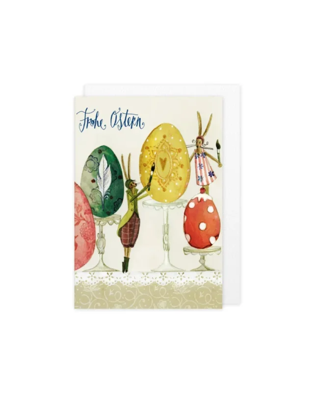 Illustration der Grußkarte „Ostern“ vom Grätz Verlag mit Hasenfiguren, kunstvoll bemalten Ostereiern auf Podesten, Schriftzug „Frohe Ostern“ und dekorativem Musterhintergrund.