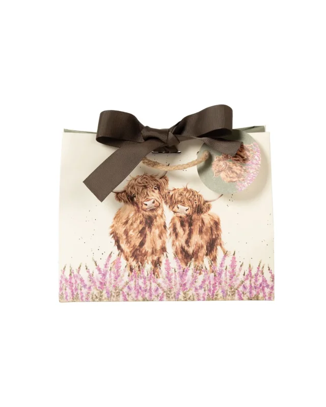 Die Geschenktasche zeigt zwei flauschige Hochlandrinder mit brauner Fellfarbe, die in einem Feld aus violett-rosanen Fingerhutblumen stehen. Im für Hannah Dale typischen natürlichen Stil blicken die beiden sanftmütig über die Blüten hinweg. Die Tasche ist am oberen Rand mit einer Schleife verschlossen. Ein Patch, welcher an der Verschlusskordel angebracht ist zeigt ebenfalls das Hochlandkuh-Motiv.
