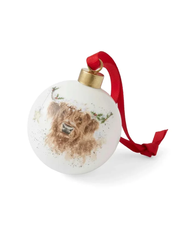 Hochlandkuh Porzellankugel "Royal Worcester Highland Star" von Wrendale Designs vor weißen Hintergrund. Das Motiv zeigt eine glückliche Hochlandkuh vor einem weihnachtlichen Hintergrund welche glücklich in die Kamera blickt.