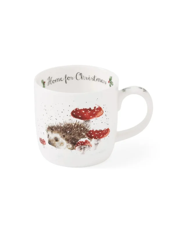 Porzellantasse mit Igel-Motiv von Wrendale Designs vor weißem Hintergrund. Innen steht „Home for Christmas“ und die Vorderseite zeigt einen Igel zwischen schneebedeckten Fliegenpilzen.