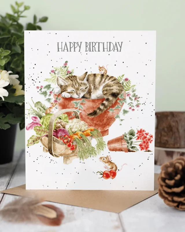 Katzen Grußkarte "Purrrfect Birthday" von Wrendale Designs illustriert von Hannah Dale. Eine braun-grau getigerte Katze liegt schlafend in einem Blumenkübel. Vorm Kübel steht ein Gemüsekorb mit Möhren, Salat, Kohl, Tomaten und weiterem Gemüse. Eine Maus hat sich bereits an den Tomaten bedient, während eine weitere auf der schlafenden Katze sitzt. Dekoriert mit Feder und Tannenzapfen und auf einem weißen Tisch aufgestellt.