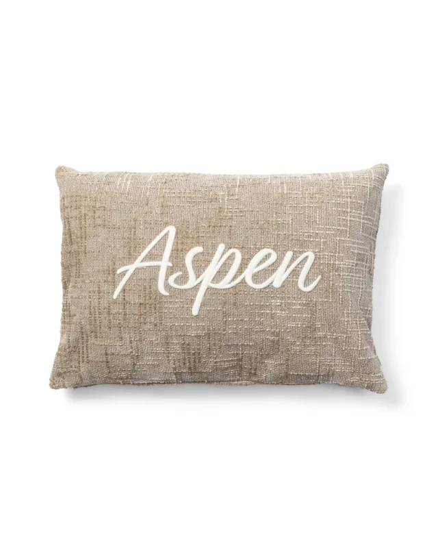 Vorderseite des beigen Kissenbezugs mit weißem „Aspen“-Schriftzug von Rivièra Maison vor weißem Hintergrund.