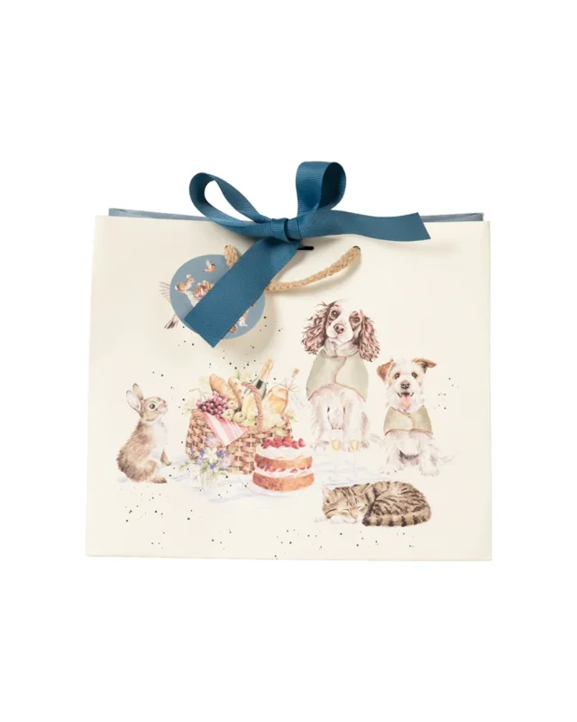 Geschenktasche "The Hoppy Picnic" von Wrendale Designs. Zu sehen ist eine Illustration von zwei Hunden mit Überwurfdeckchen und ein Kaninchen sitzend auf einer Picknickdecke. Vor der Picknickdecke liegt eine braun-schwarz getigerte schlafende Katze. Ein niedliches Rotkehlchen fliegt über die Picknickdecke hinweg, auf welcher sich ein prall gefüllter Picknickkorb und ein Erbeerkuchen befinden.