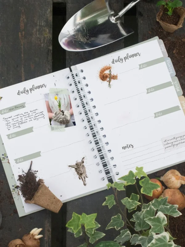 Aufgeschlagenes Gardening Journal von Wrendale Designs mit Tagesplanung, Notizseiten und Gartenmotiven auf Holztisch