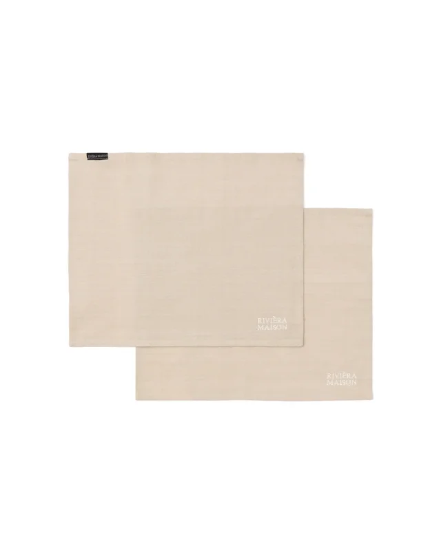 Freigestelltes Bild der RM Classic Placemat Platzsets von Rivièra Maison im 2er-Set, schlicht in Beige mit gesticktem Logo vor weißem Hintergrund.