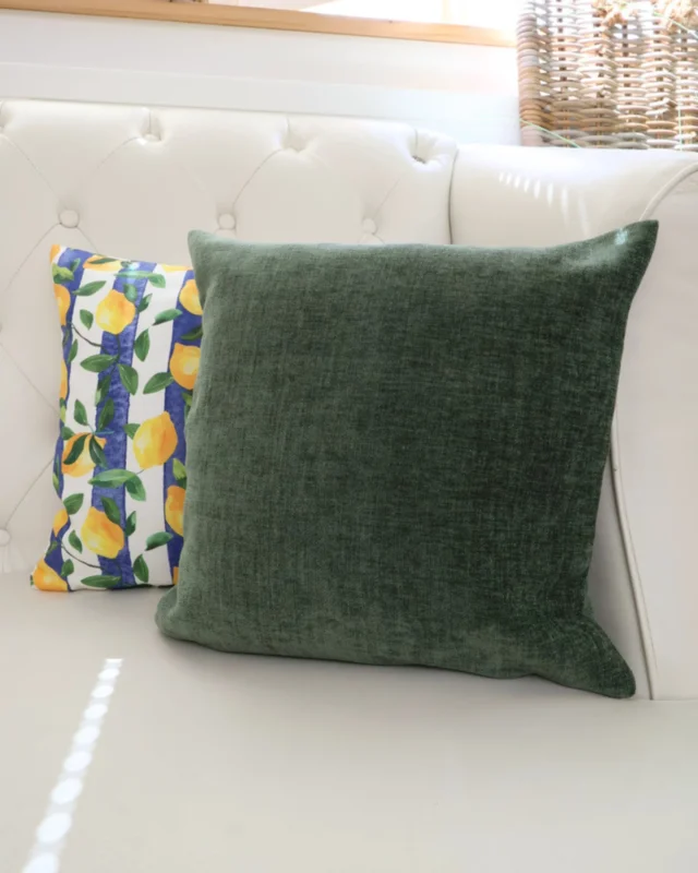Dekoiertes Bild des Kissens "Kensington". Das Kissen ist simpel mit einem edlen Grünton gestaltet. Es liegt neben dem "Lemontree" auf einem weißen Sofa.