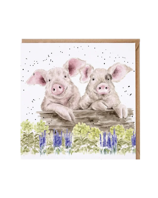 Doppelkarte mit niedlichen Schweinen von Wrendale Designs. Zwei Schweine blicken freundliche über einen Holzblalken hinweg, welcher auf einer Blühwiese liegt. Blaue und gelbe Blüten sind von Hannah Dale dargestellt.