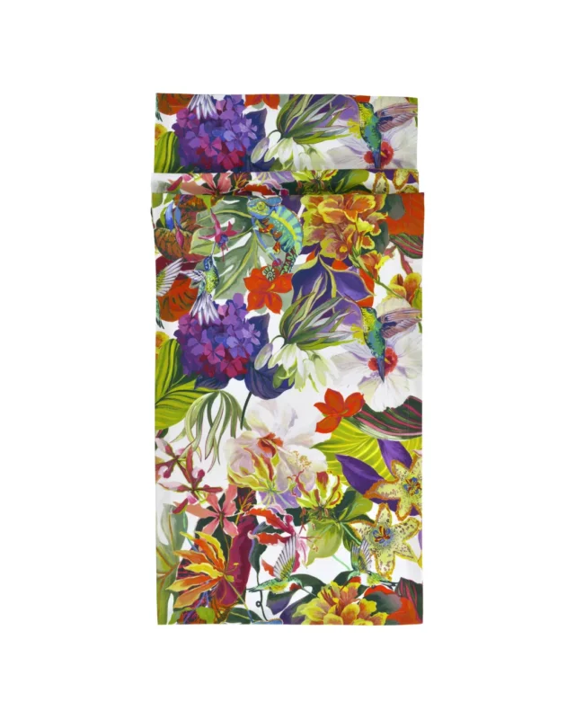 Auf diesem Tischläufer ist ein detailreiches Muster aus üppigen Palmen, exotischen Blüten, mehreren Kolibris, Orchideen und einem Chamäleon in knalligen Farben wie Pink, Orange und Blau auf cremefarbenem Hintergrund abgebildet. Der Tischläufer besteht aus Baumwolle und ist in zwei Größen erhältlich.
