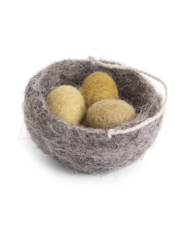 Graues Filz-Vogelnest mit drei gelben Filzeiern als Osteranhänger, freigestellt vor weißem Hintergrund.
