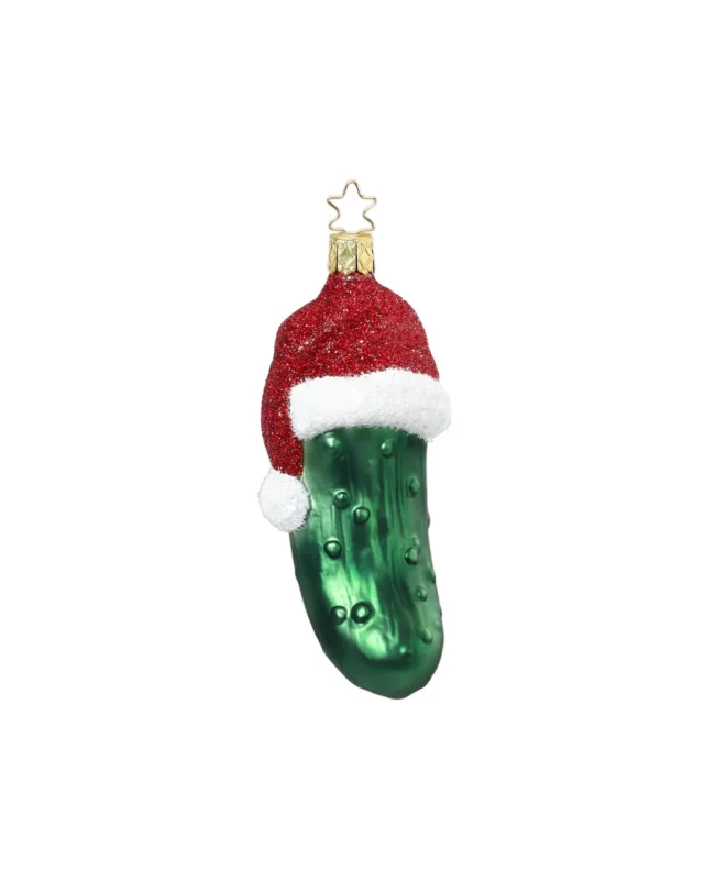 In Deutschland handgefertigter Weihnachtsbaumschmuck Weihnachtsgurke mit Mütze. Die grüne Gurke trägt eine weiß-rote Weihnachtsmütze mit Bommel und rotem Glitzer.