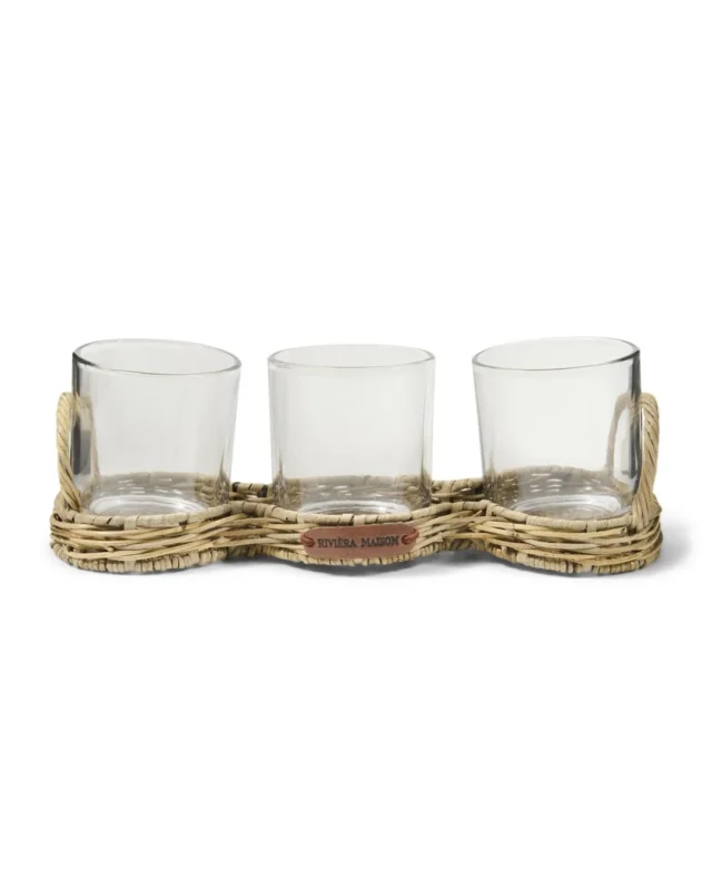Rustic Rattan Windlicht "Triple Voltive" von Riviera Maison vor weißen Hintergrund. Das Windlicht besteht aus einer Rustic Rattan Basis und 3 Gläsern welche perfekt in die Basis passen. An der Seite steht die Aufschrift "Riviera Maison".