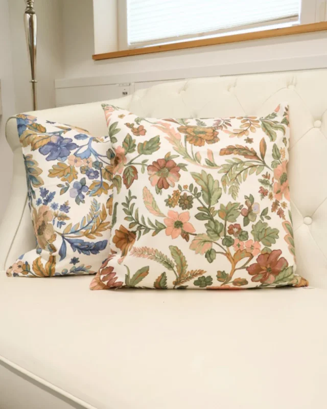 Zwei florale Kissen "Ravenna" in blau und rosa von Sander. Das Motiv zeigt ein florales Design. Die Kissen liegen auf einem weißen Sofa.