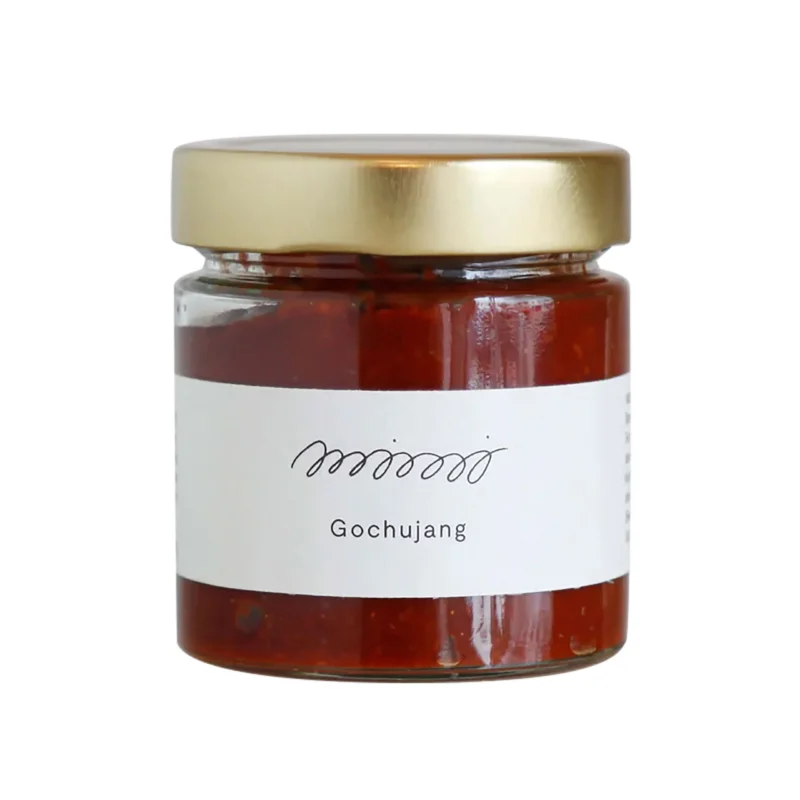 Bio Gochujang - koreanische Chilipaste im Glas mit goldenem Deckel und weißem Etikett auf weißem Hintergrund.